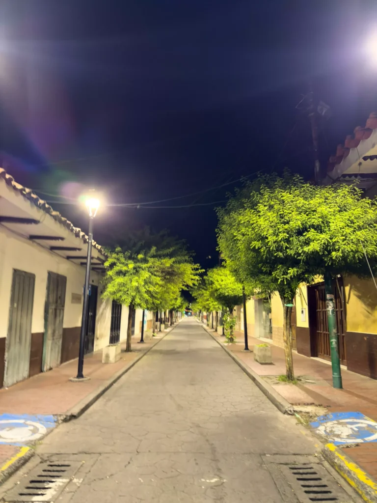 Calle iluminada con árboles y edificios coloniales en el centro histórico de Buga por la noche, un encanto local.
