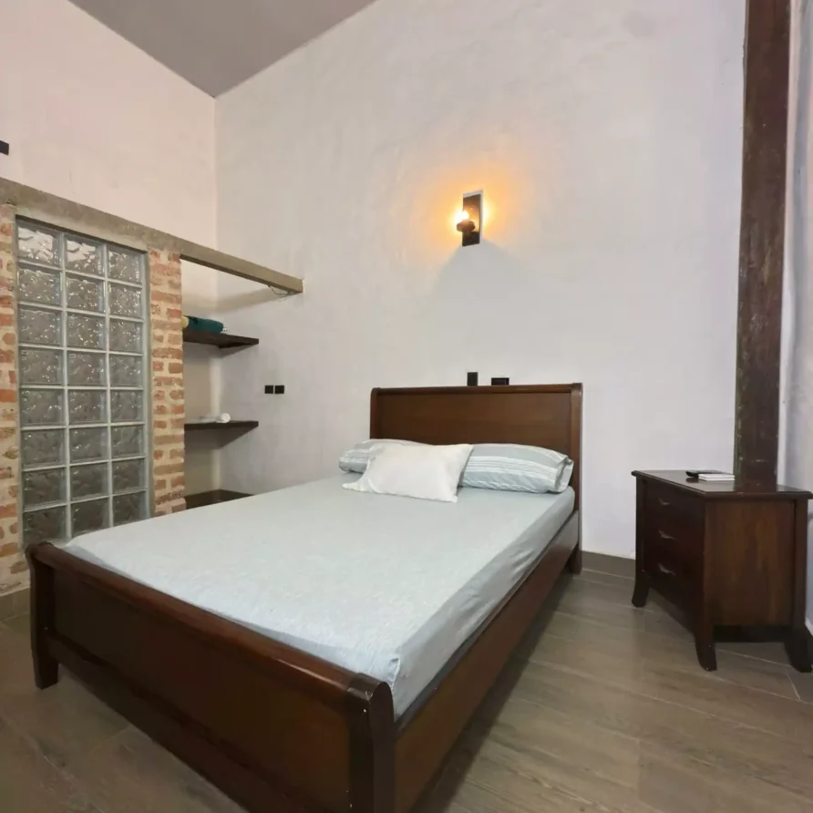 Dormitorio de hotel acogedor con cama de madera, sábanas celestes y mesita de noche, ideal para hotel Casa Encanto en Buga.