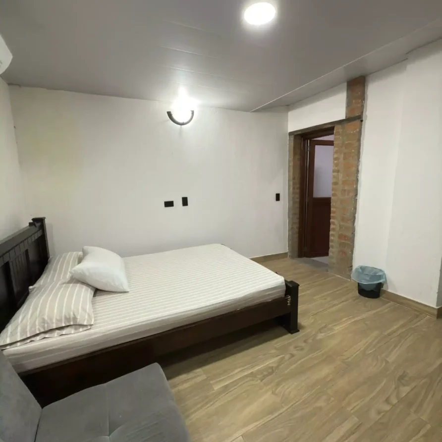 Interior de habitación de hotel con cama de madera, suelo de parquet y luz cálida, en Buga, próximo a la Basílica.