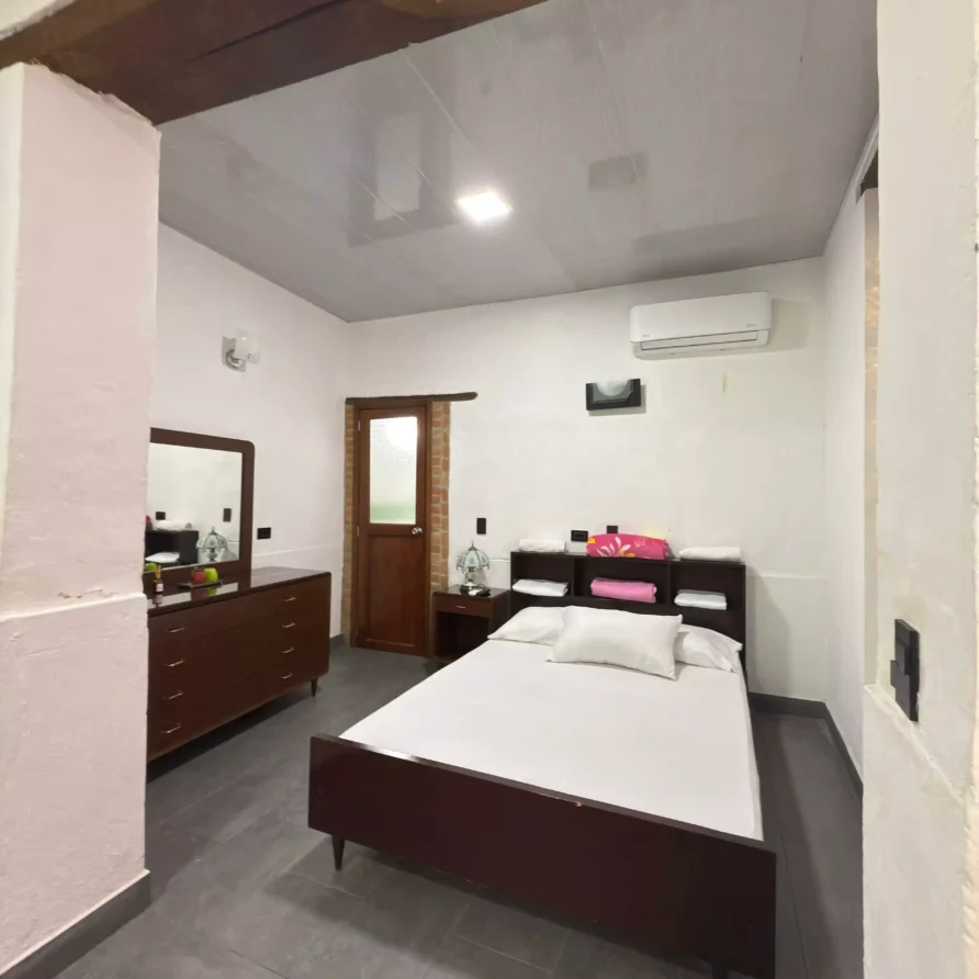 Habitación de hotel acogedora con cama, tocador de madera y aire acondicionado, ideal para descansar en Buga.
